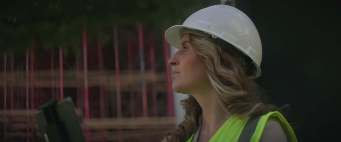 A construction worker uses a handheld electronic device while standing outside a building