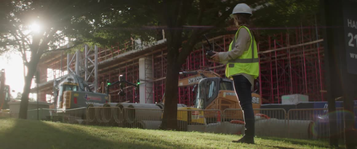 Construction worker wearing hardhat controlling a drone near a building
