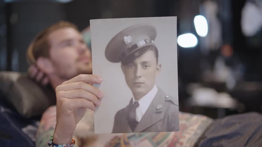 Young shirtless tattooed man shows a vintage photo of a soldier