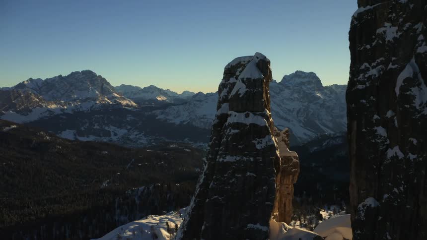 Aerial view of the sun setting over the snow covered slopes of a mountain range