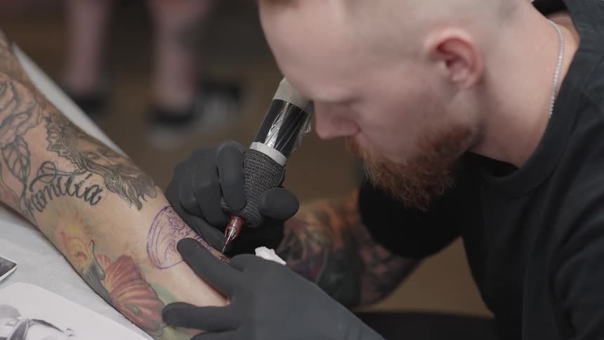 A tattoo artist works on a small section of a larger piece on a mans arm