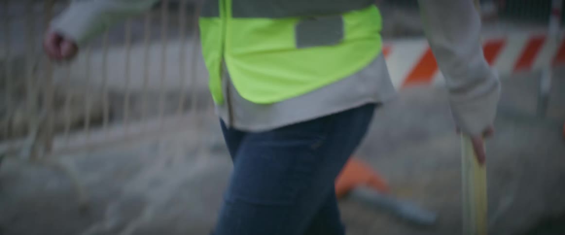 A woman holding blueprints is walking around a construction area in a city