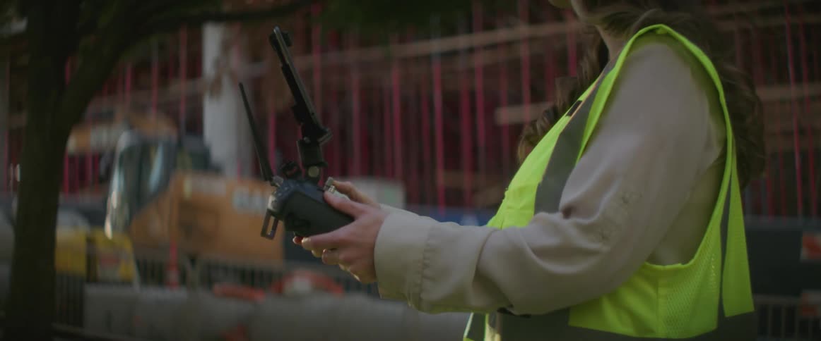 A woman is holding some electronic equipment in front of a building under construction