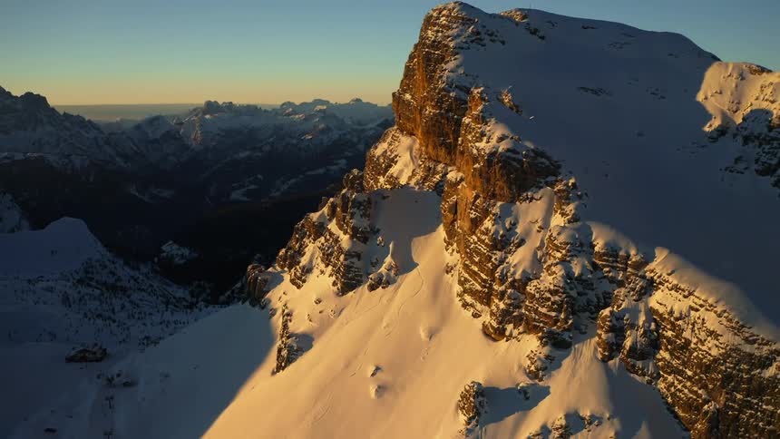 Aerial view of snow covering the peaks of a mountain range at sunset