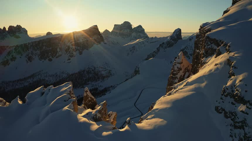 An aerial view of snowy mountains with the sun setting in the distance during the winter