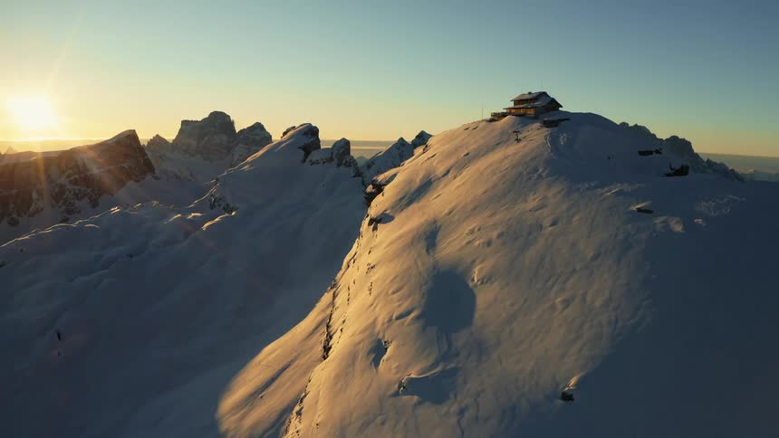 Snow covered mountain range under a clear sky and a bright sun on the horizon