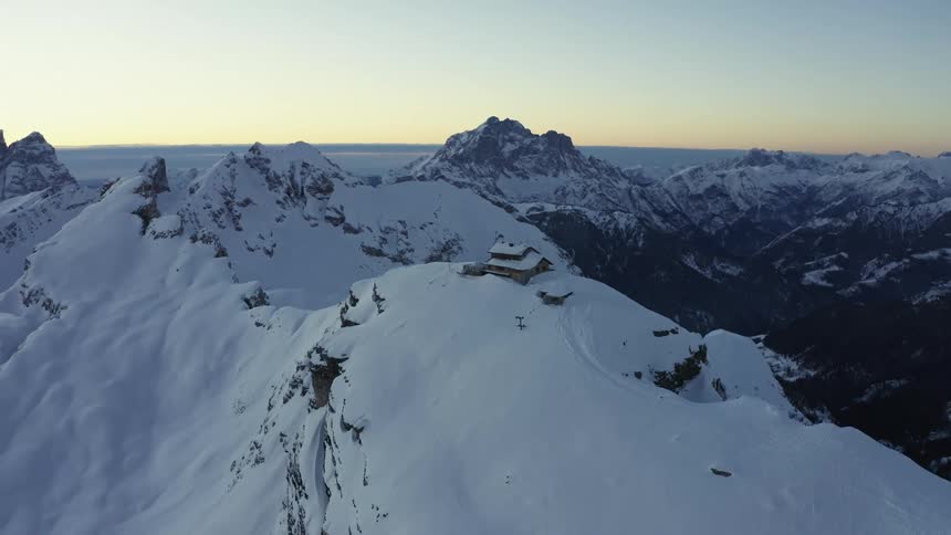 A mountain range with a house covered in snow and ice with the sky and clouds in the background