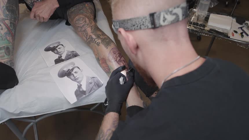 Tattoo artist copying a vintage old timey photograph of a soldier on a clients leg