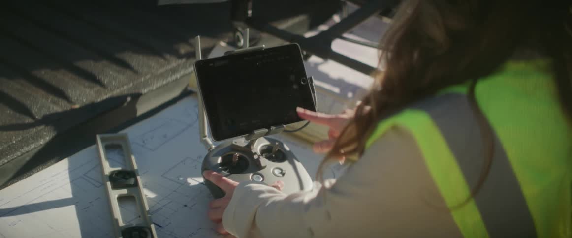 Female construction worker wearing construction work clothes using the touchscreen on a drone remote control
