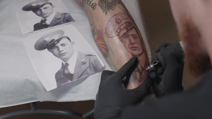 Tattoo artist creates tattoo on clients limb based on photo of man in uniform
