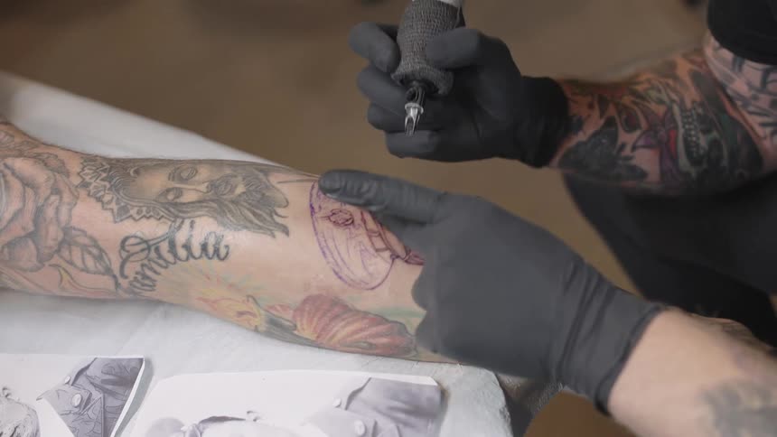 A tattoo artist is drawing a tattoo of a mans face on a persons leg