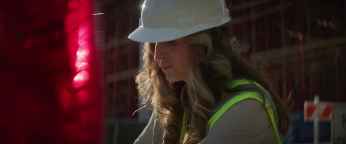 A woman with a hardhat and a vests looking at blueprints in the back of a pickup truck