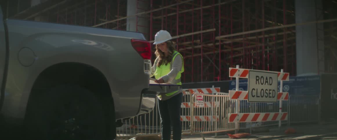 A woman with a hardhat and a vests looking at blueprints in the back of a pickup truck