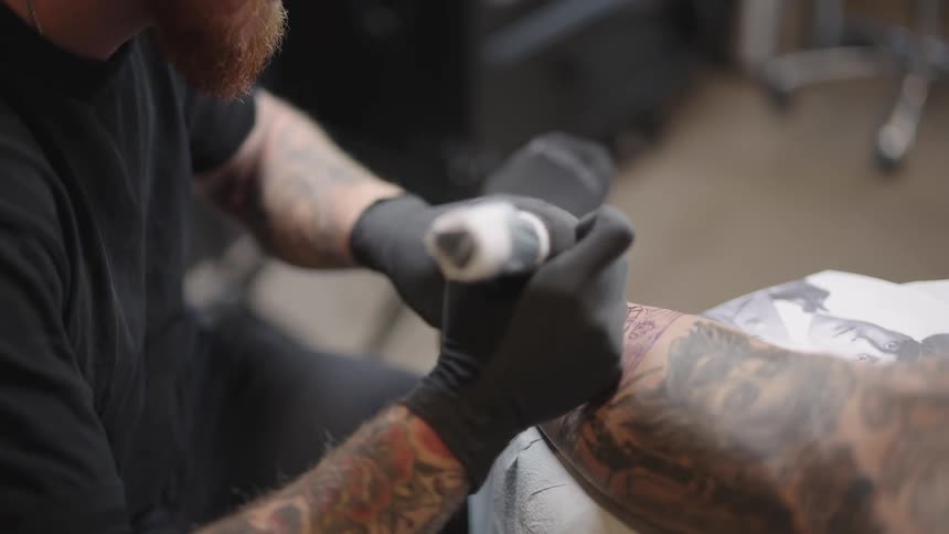 A tattoo artist feels a mans leg and then starts to tattoo on it