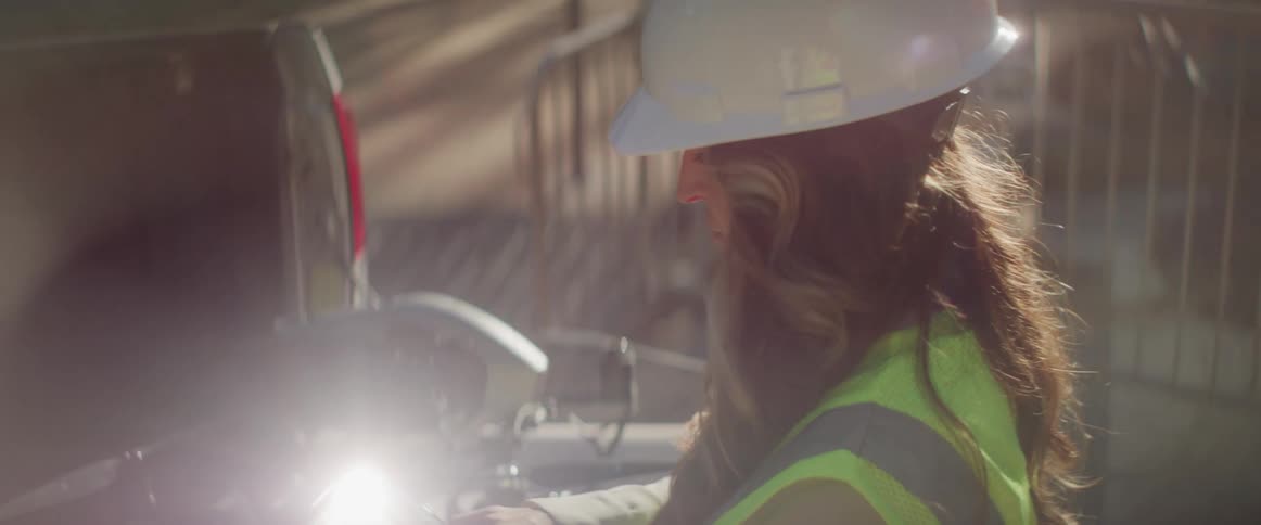 A female construction worker is standing at a work table typing on her phone