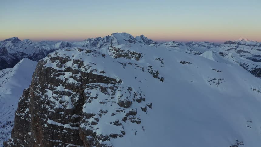 A cross standing atop a snowy mountain peak in the evening