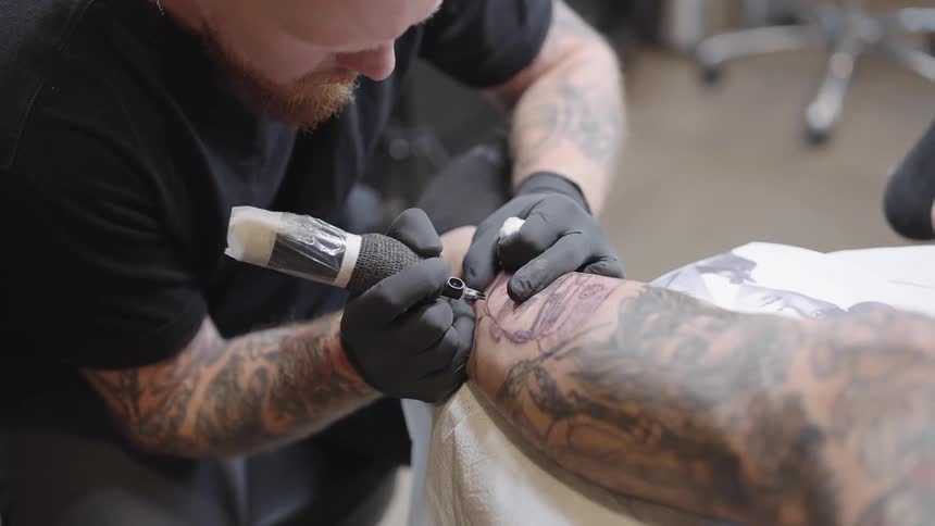 A tattoo artist is giving a man a tattoo on his arm