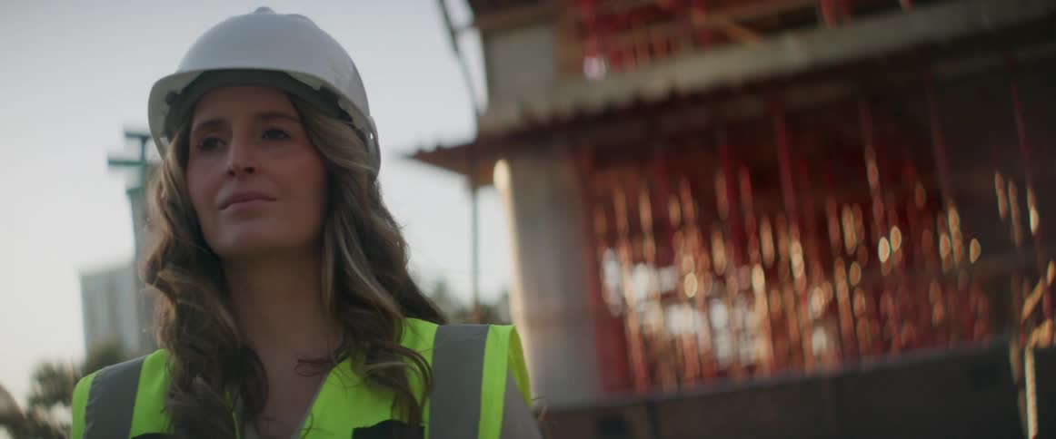 A woman standing at a construction site wearing a hardhat and reflective vest