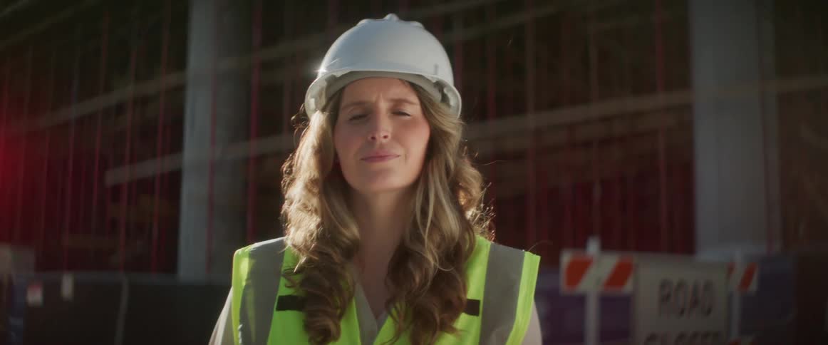 A female construction looks into the camera while standing on a construction site