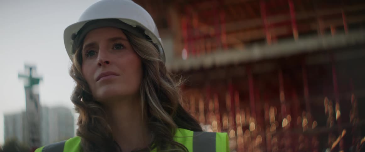 A female construction worker wearing a hard hat is standing in front of construction site