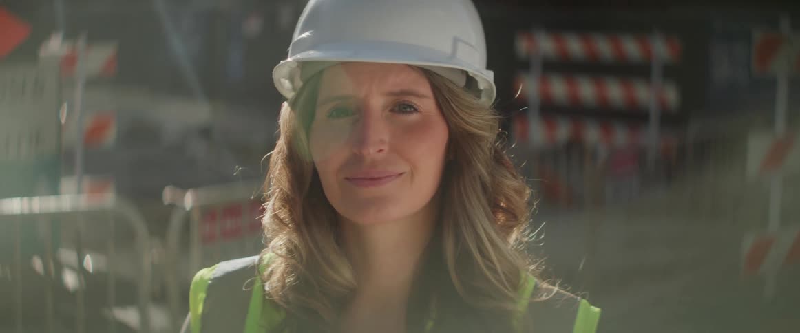 A woman with a hard hat stands at a construction site