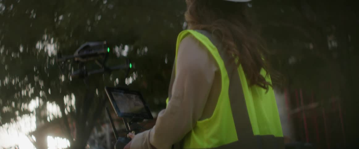 A female construction worker is wearing a hard hat and operating a drone