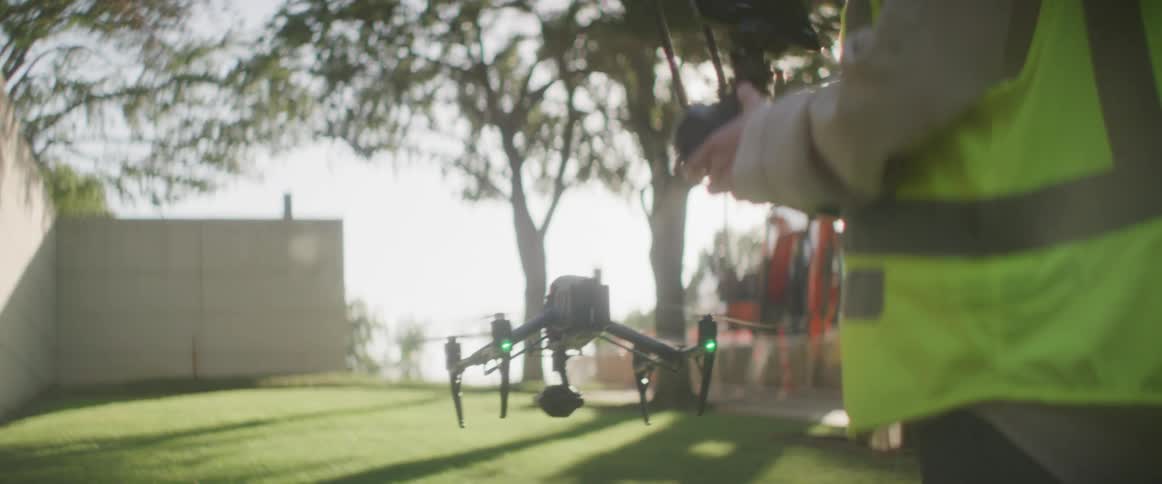 Construction worker controlling a drone near a construction site at morning