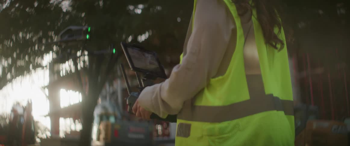 Construction worker wearing white hardhat controlling a drone near a building