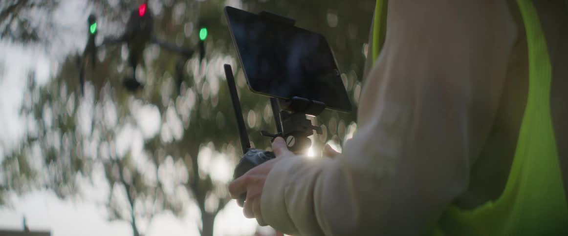 A female construction worker is wearing a hard hat and operating a drone