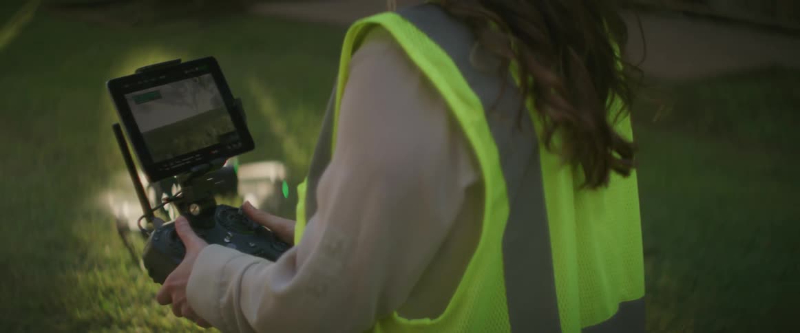 A female construction worker is standing outside operating a drone