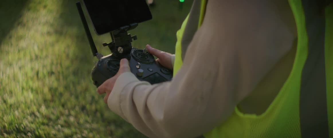 A female construction worker is standing outside operating a drone