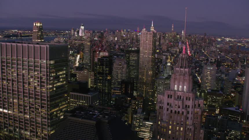 An aerial view of a metropolis at dusk with glowing lights from the windows of the many windows