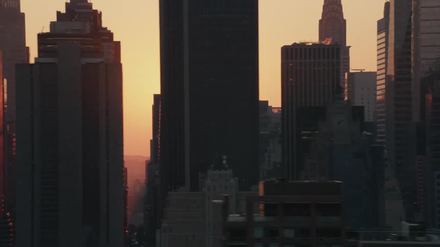 A bright orange sun shines though a skyline of tall buildings and skyscrapers