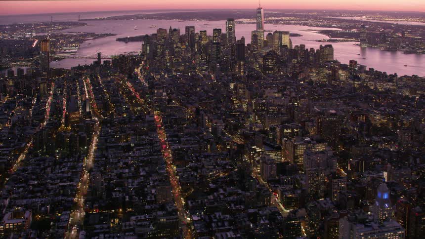 Aerial view of illuminated tall buildings with skyscrapers next to river at dawn in the city
