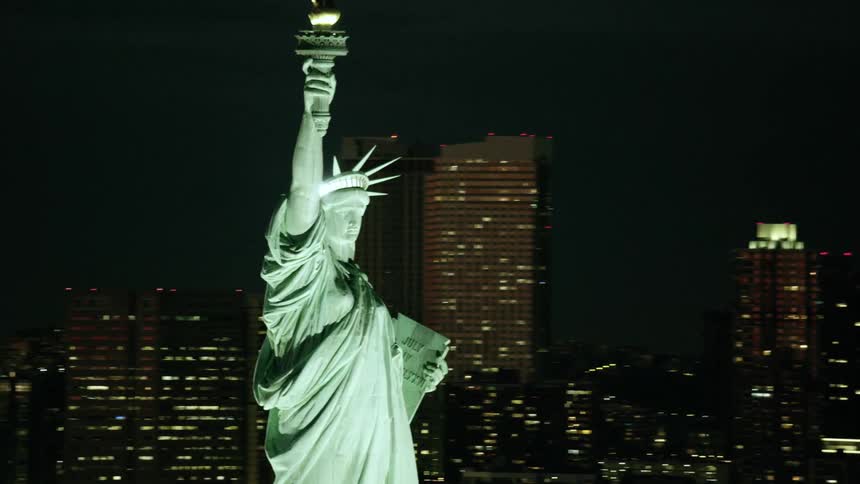 The statue of liberty in front of lit up buildings in new york city at night