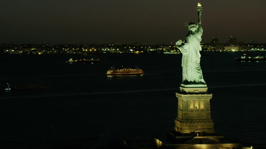 Aerial view of the statue of liberty in front of the new york city skyline at night
