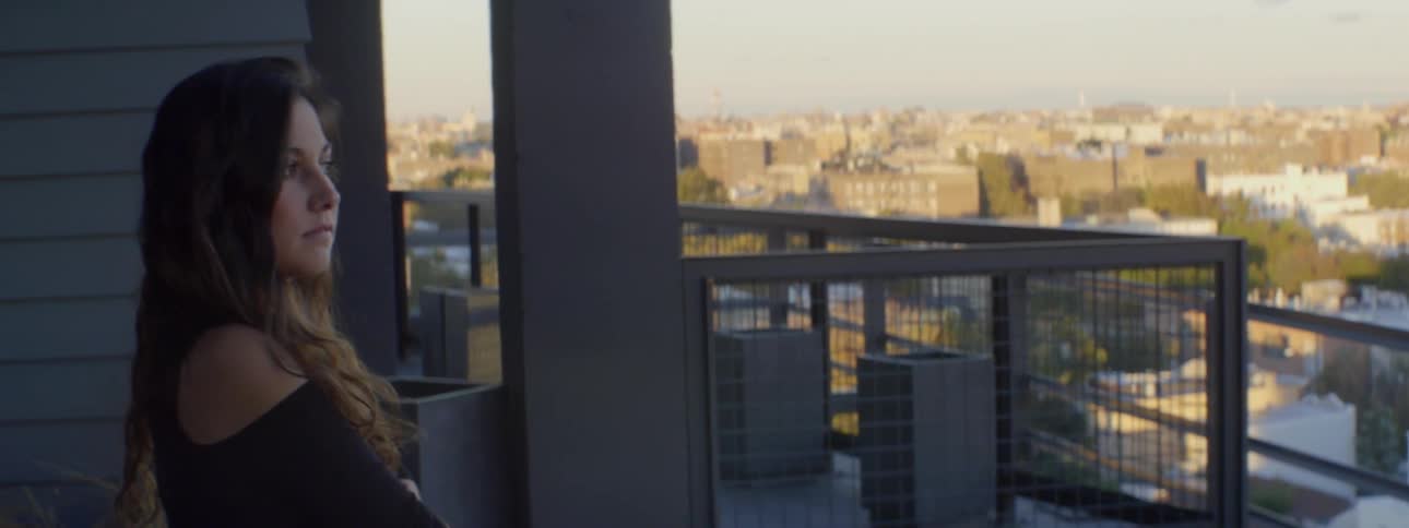 Woman looking out a window and then walking across the room in a big city