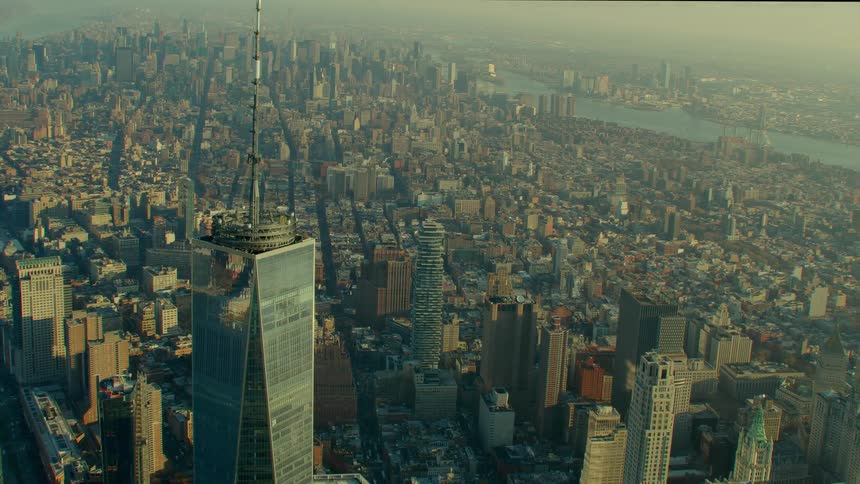 The spire on top of a skyscraper stands high above a big city under a hazy sky