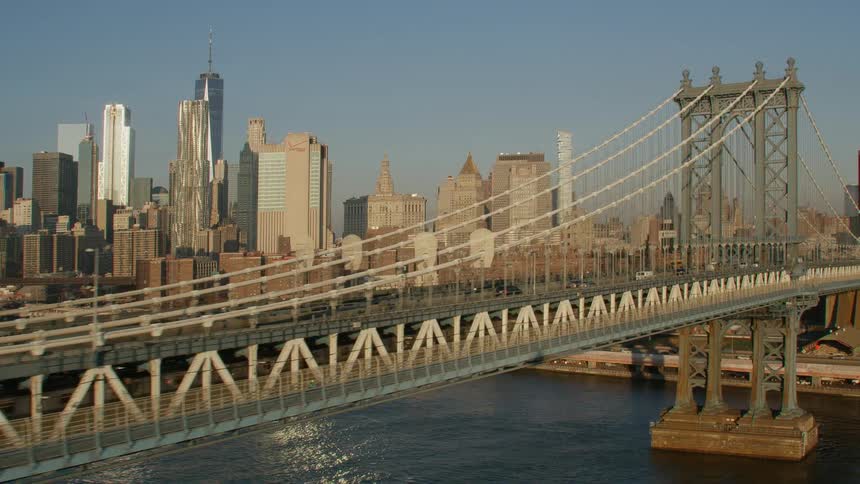 Cars travel across a bridge to a big city with tall skyscrapers high in a clear blue sky