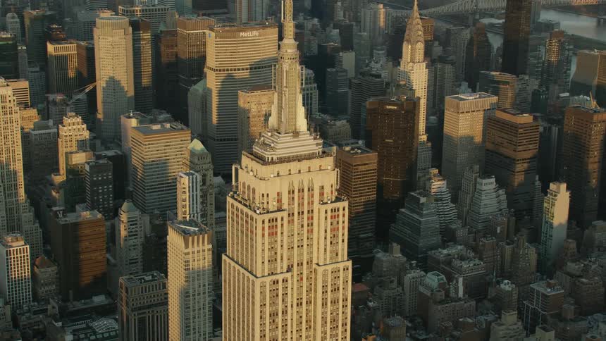 Sunlight shines on a tall city building with a spire high in the sky surrounded by other buildings