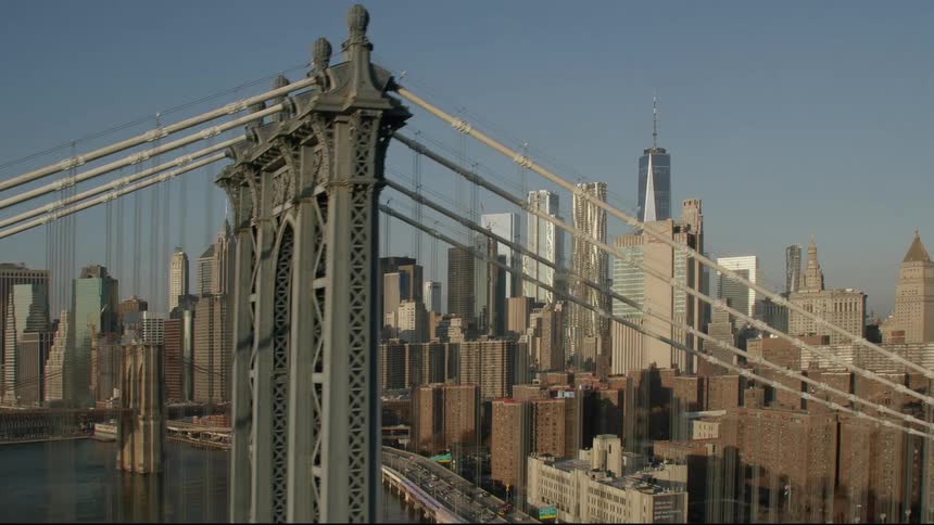 Cars travel across a bridge over a river to a big city with tall skyscrapers and buildings