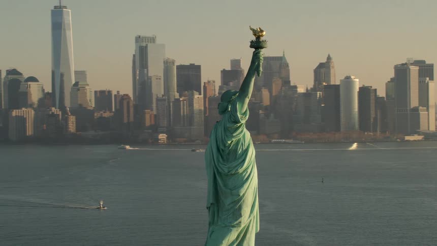The statue of liberty in front of the new york city skyline at sunset