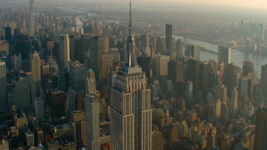Aerial view of skyscaper with spire and tall buildings next to river at dawn in the city