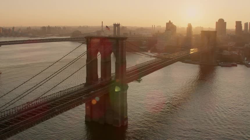 Sun shines through city onto suspension bridge turning skyscrapers into silhouettes