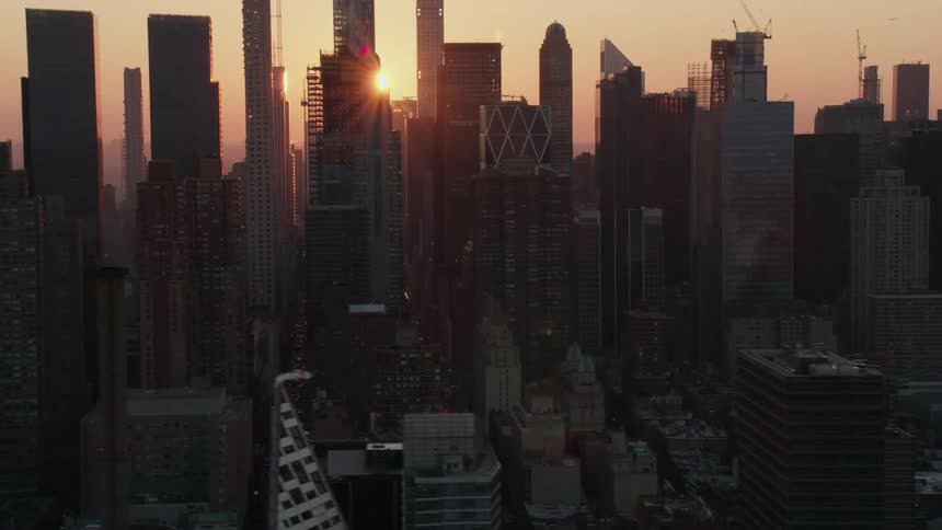 A bright orange sun shines though a skyline of tall buildings and skyscrapers