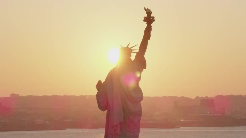 The statue of liberty standing in the new york bay at sunset