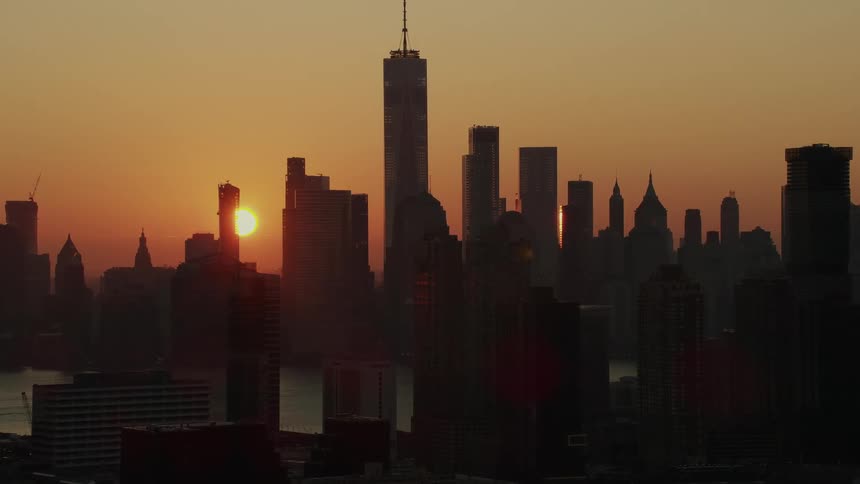 The sun rises over a city with skyscrapers on both sides of a river