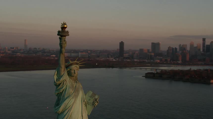 The statue of liberty holds her torch high with new york harbor and the city in the background