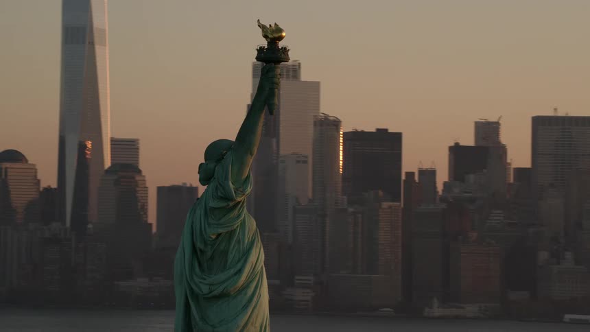 Statue of liberty stands across from skyscrapers under a red sky