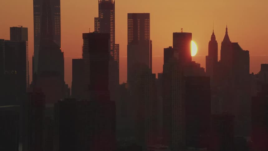 The setting sun peaks between skyscrapers in a metropolis
